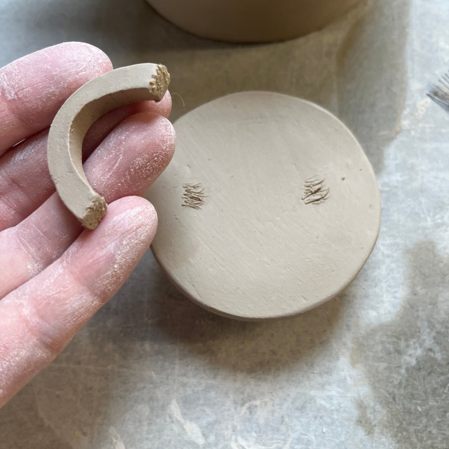 Close-up of a handmade teapot lid with a partially attached clay handle, showcasing the hand-building pottery process. Perfect for illustrating craftsmanship and DIY pottery techniques for teapot-making templates available in the store.